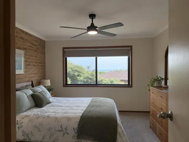 Bedroom with ceiling fan over a bed, window and dresser in a carpeted home in The Entrance