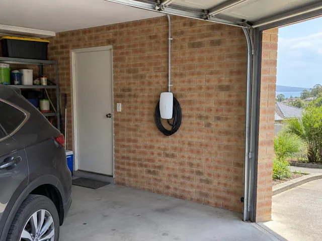 Wall-mounted EV charger on a brick garage wall beside a door in a home garage in Shelly Beach